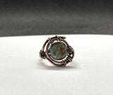 This handcrafted ring features a vibrant African green opal wrapped in warm copper. The stone’s natural patterns and earthy green tones are enhanced by the copper setting, creating a bold yet elegant design. Sized at 6, this ring is a unique piece that carries both natural beauty and artisan craftsmanship.