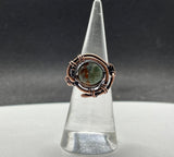 This handcrafted ring features a vibrant African green opal wrapped in warm copper. The stone’s natural patterns and earthy green tones are enhanced by the copper setting, creating a bold yet elegant design. Sized at 6, this ring is a unique piece that carries both natural beauty and artisan craftsmanship.