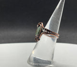 This handcrafted ring features a vibrant African green opal wrapped in warm copper. The stone’s natural patterns and earthy green tones are enhanced by the copper setting, creating a bold yet elegant design. Sized at 6, this ring is a unique piece that carries both natural beauty and artisan craftsmanship.