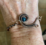 This Lovely Blue Apatite and Wire Wrapped Copper Wave Bracelet is a stunning piece of jewelry featuring vibrant blue apatite stones set against an intricate copper wave design. The bracelet combines the natural beauty of apatite with the elegance of wire-wrapped copper to create a unique and eye-catching accessory.