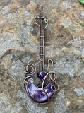 This Rock n’ Roll Lepidolite Moon Guitar Pendant is a distinctive and edgy piece of jewelry that combines the charm of lepidolite with the playful design of a guitar-shaped pendant. The pendant is crafted in copper and features an amethyst bead accent, adding a touch of elegance and color to the bold design.