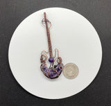 This Rock n’ Roll Lepidolite Moon Guitar Pendant is a distinctive and edgy piece of jewelry that combines the charm of lepidolite with the playful design of a guitar-shaped pendant. The pendant is crafted in copper and features an amethyst bead accent, adding a touch of elegance and color to the bold design.