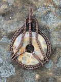This stunning Crazy Lace Agate pendant showcases intricate copper wire wrapping. The agate's vibrant patterns are beautifully highlighted by the handwoven copper, creating a distinctive and eye-catching piece. The detailed craftsmanship enhances the natural beauty of the stone, making it a unique addition to any jewelry collection.