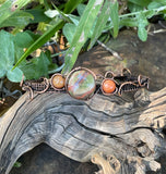 This handcrafted bracelet features a harmonious blend of earthy Rainforest Jasper and vibrant Carnelian, wrapped in warm copper wire. The adjustable design ensures a comfortable fit, while the copper wirework enhances the natural beauty of the stones.
