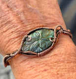 This cuff bracelet features a beautifully carved labradorite stone, known for its magical flashes of blue, green, and gold. The stone is securely wrapped in rich, handwoven copper wire, forming a bold and elegant cuff that radiates both strength and mystique.