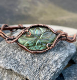 This cuff bracelet features a beautifully carved labradorite stone, known for its magical flashes of blue, green, and gold. The stone is securely wrapped in rich, handwoven copper wire, forming a bold and elegant cuff that radiates both strength and mystique.