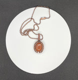 This eye-catching necklace features a shimmering Goldstone centerpiece, known for its rich, warm hue and subtle sparkle. Wrapped in handcrafted copper wire and surrounded by copper beads, the setting enhances the stone's radiant glow while adding a rustic, artisanal charm. A striking piece that blends elegance with earthy warmth.