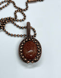 This eye-catching necklace features a shimmering Goldstone centerpiece, known for its rich, warm hue and subtle sparkle. Wrapped in handcrafted copper wire and surrounded by copper beads, the setting enhances the stone's radiant glow while adding a rustic, artisanal charm. A striking piece that blends elegance with earthy warmth.