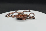 This eye-catching necklace features a shimmering Goldstone centerpiece, known for its rich, warm hue and subtle sparkle. Wrapped in handcrafted copper wire and surrounded by copper beads, the setting enhances the stone's radiant glow while adding a rustic, artisanal charm. A striking piece that blends elegance with earthy warmth.