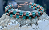 This handcrafted bracelet features rich copper wire, artistically coiled to create texture and movement, accented with vibrant teal-colored glass beads. The warm copper beautifully contrasts the cool, refreshing tones of the beads, making this piece both bold and elegant. Perfect for adding a pop of color and artisan flair to any outfit.