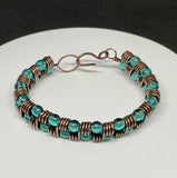 This handcrafted bracelet features rich copper wire, artistically coiled to create texture and movement, accented with vibrant teal-colored glass beads. The warm copper beautifully contrasts the cool, refreshing tones of the beads, making this piece both bold and elegant. Perfect for adding a pop of color and artisan flair to any outfit.