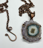 This Purple, Brown, Green, and White Stalactite Slice Necklace features a beautifully natural stalactite slice adorned with a variety of colors including purple, brown, green, and white, all set in copper. This necklace highlights the unique geological beauty of stalactites and the craftsmanship of copper jewelry.