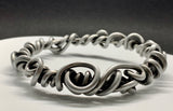 Crafted from over 6 feet of heavy-duty 8-gauge antiqued aluminum wire, this bold bangle bracelet features an intricate swirl design that’s both durable and lightweight. The antiqued finish adds depth and character.