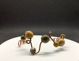 This unique bracelet is handcrafted from heavy gauge copper, shaped and curved into an organic freeform design. Accented with Picasso Jasper beads, known for their intricate natural patterns and earthy tones, The warm hues of the copper beautifully complement the stone’s striking marbled appearance. A bold statement bracelet for those who appreciate artisan craftsmanship and nature-inspired jewelry.