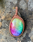 This pendant showcases a rainbow quartz cabochon, dyed in stunning pastel shades that shimmer softly in the light. The stone is gracefully encased in handwoven polished copper, adding warmth and intricate detail to the design. A perfect accessory for those who appreciate unique, handcrafted jewelry with a playful yet elegant touch.