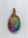 This pendant showcases a rainbow quartz cabochon, dyed in stunning pastel shades that shimmer softly in the light. The stone is gracefully encased in handwoven polished copper, adding warmth and intricate detail to the design. A perfect accessory for those who appreciate unique, handcrafted jewelry with a playful yet elegant touch.
