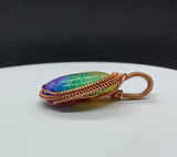 This pendant showcases a rainbow quartz cabochon, dyed in stunning pastel shades that shimmer softly in the light. The stone is gracefully encased in handwoven polished copper, adding warmth and intricate detail to the design. A perfect accessory for those who appreciate unique, handcrafted jewelry with a playful yet elegant touch.