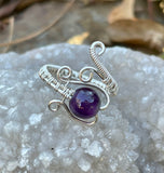 This ring showcases a radiant Amethyst gemstone with an wire wrapped sterling silver wire band. The adjustable band fits ring sizes 7 to 11, making it a versatile piece for various finger sizes. The deep purple Amethyst, known for its spiritual and healing qualities, creates a captivating focal point that contrasts beautifully with the sleek silver wire. Perfect for any occasion, this ring combines timeless style with comfort and ease of wear.