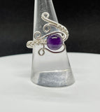This ring showcases a radiant Amethyst gemstone with an wire wrapped sterling silver wire band. The adjustable band fits ring sizes 7 to 11, making it a versatile piece for various finger sizes. The deep purple Amethyst, known for its spiritual and healing qualities, creates a captivating focal point that contrasts beautifully with the sleek silver wire. Perfect for any occasion, this ring combines timeless style with comfort and ease of wear.