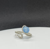 This elegant ring features a stunning Blue Chalcedony gemstone, wrapped in wire with Argentium Silver for a refined and durable finish. The ring is adjustable, accommodating sizes 5 to 8, ensuring a perfect fit for any finger. The soft blue hue of the chalcedony contrasts beautifully with the bright, shiny silver, creating a sophisticated and versatile piece that can complement any style.