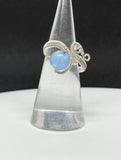 This elegant ring features a stunning Blue Chalcedony gemstone, wrapped in wire with Argentium Silver for a refined and durable finish. The ring is adjustable, accommodating sizes 5 to 8, ensuring a perfect fit for any finger. The soft blue hue of the chalcedony contrasts beautifully with the bright, shiny silver, creating a sophisticated and versatile piece that can complement any style.