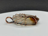 This Dark Brown to Clear Agate Tree of Life Pendant is a stunning piece of boho-inspired jewelry featuring a natural agate stone with a gradient from dark brown to clear. The pendant is beautifully wrapped in copper and showcases a detailed Tree of Life design, making it a unique and nature-inspired accessory.