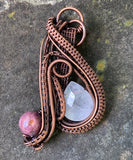 This captivating pendant features a sparkling faceted Rose Quartz teardrop paired with a rich purple Agate bead, both artfully framed by layers of woven copper. The intricate wirework enhances the natural beauty of each stone, creating a harmonious blend of soft pinks and purples against the warm copper. A statement piece for those who appreciate fine craftsmanship and the gentle allure of gemstones.