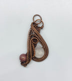 This captivating pendant features a sparkling faceted Rose Quartz teardrop paired with a rich purple Agate bead, both artfully framed by layers of woven copper. The intricate wirework enhances the natural beauty of each stone, creating a harmonious blend of soft pinks and purples against the warm copper. A statement piece for those who appreciate fine craftsmanship and the gentle allure of gemstones.