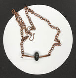 This earthy necklace features a naturally tumbled black river rock, carefully drilled and set in a heavy gauge, hammered copper mounting. The raw textures and grounding tones of the stone are beautifully contrasted by the rich, rustic warmth of the copper. A tribute to nature’s simplicity and strength—perfect for those who appreciate organic, one-of-a-kind design with a touch of rugged charm.