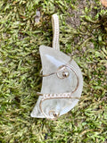 This pendant showcases a luminous quartz crystal carved into a delicate moon shape, beautifully encased in handwoven sterling (.925) and fine (.999) silver wire. The intricate silver weaving highlights the crystal’s natural clarity and gentle glow, creating a piece that is both mystical and elegant.