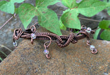 This eye-catching bracelet showcases a stunning combination of woven copper, intricate copper swirls, and shimmering iridescent glass bead dangles. The rich, warm tones of the copper beautifully complement the radiant beads, creating a unique artistic design. Handcrafted with care, this bracelet is perfect for those who love bold, statement jewelry with a touch of whimsical sparkle.