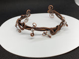 This eye-catching bracelet showcases a stunning combination of woven copper, intricate copper swirls, and shimmering iridescent glass bead dangles. The rich, warm tones of the copper beautifully complement the radiant beads, creating a unique artistic design. Handcrafted with care, this bracelet is perfect for those who love bold, statement jewelry with a touch of whimsical sparkle.