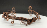 This eye-catching bracelet showcases a stunning combination of woven copper, intricate copper swirls, and shimmering iridescent glass bead dangles. The rich, warm tones of the copper beautifully complement the radiant beads, creating a unique artistic design. Handcrafted with care, this bracelet is perfect for those who love bold, statement jewelry with a touch of whimsical sparkle.