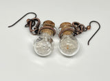 These whimsical earrings feature tiny glass bottles wrapped in warm copper, each filled with a mix of clear and light smoky quartz tumbles. Hanging from hypoallergenic niobium ear wires, they’re lightweight, playful, and full of earthy charm. A unique design that combines craftsmanship with a touch of crystal magic.