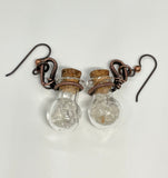 These whimsical earrings feature tiny glass bottles wrapped in warm copper, each filled with a mix of clear and light smoky quartz tumbles. Hanging from hypoallergenic niobium ear wires, they’re lightweight, playful, and full of earthy charm. A unique design that combines craftsmanship with a touch of crystal magic.
