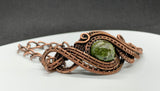 This Copper Ore Jasper Bracelet features a stunning Copper Ore Jasper stone as its focal point, surrounded by intricate, rolling hand-woven copper weaves. The bracelet combines the natural beauty of the jasper stone with the warmth and artistry of copper wirework, creating a bold and elegant accessory that showcases skilled craftsmanship. The earthy tones of the stone paired with the flowing copper design make this a striking and versatile piece.