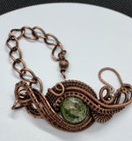 This Copper Ore Jasper Bracelet features a stunning Copper Ore Jasper stone as its focal point, surrounded by intricate, rolling hand-woven copper weaves. The bracelet combines the natural beauty of the jasper stone with the warmth and artistry of copper wirework, creating a bold and elegant accessory that showcases skilled craftsmanship. The earthy tones of the stone paired with the flowing copper design make this a striking and versatile piece.