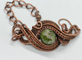 This Copper Ore Jasper Bracelet features a stunning Copper Ore Jasper stone as its focal point, surrounded by intricate, rolling hand-woven copper weaves. The bracelet combines the natural beauty of the jasper stone with the warmth and artistry of copper wirework, creating a bold and elegant accessory that showcases skilled craftsmanship. The earthy tones of the stone paired with the flowing copper design make this a striking and versatile piece.