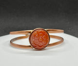 This beautiful bangle bracelet features a vibrant Carnelian stone intricately carved into a delicate flower, accentuating the stone’s natural warm hues. The flower is set on a handcrafted copper bangle, adding an earthy elegance and timeless charm. Perfect for nature lovers and those who appreciate artisanal jewelry, this bracelet makes a lovely statement piece with its warm colors and unique design.