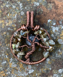 This Handmade Copper Tree Pendant is a beautifully crafted, nature-inspired piece that showcases the artisan’s skill in working with copper and natural stones. The pendant features a tree of life design, using heavy gauge copper to form the frame, while the leaves are made from Labradorite chips. A Larvikite Moon adds a celestial element, making this piece a stunning combination of nature and spirituality.