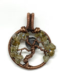 This Handmade Copper Tree Pendant is a beautifully crafted, nature-inspired piece that showcases the artisan’s skill in working with copper and natural stones. The pendant features a tree of life design, using heavy gauge copper to form the frame, while the leaves are made from Labradorite chips. A Larvikite Moon adds a celestial element, making this piece a stunning combination of nature and spirituality.