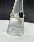 This captivating ring showcases the natural beauty of raw Quartz and raw Moldavite, set in sterling silver for a rustic yet elegant look. The adjustable band fits sizes 6 ½ and up, offering versatility and comfort. The clear, uncut Quartz radiates purity, while the rare, deep green Moldavite adds a touch of otherworldly mystique. Together, these stones are believed to enhance spiritual growth and energy. Perfect for those who appreciate raw, organic beauty, this ring is a unique and powerful statement piece