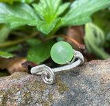 This stunning adjustable ring showcases a vibrant apple-green Prehnite gemstone, elegantly wrapped in intricate Argentium silver wire. The delicate wire weaving enhances the natural beauty and translucence of the Prehnite, creating a harmonious blend of soft green hues and shimmering silver. The adjustable band ensures a comfortable fit. A perfect piece for those who love unique, handcrafted jewelry with a pop of color!