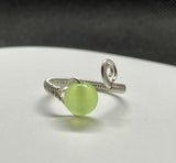 This stunning adjustable ring showcases a vibrant apple-green Prehnite gemstone, elegantly wrapped in intricate Argentium silver wire. The delicate wire weaving enhances the natural beauty and translucence of the Prehnite, creating a harmonious blend of soft green hues and shimmering silver. The adjustable band ensures a comfortable fit. A perfect piece for those who love unique, handcrafted jewelry with a pop of color!