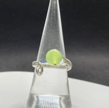 This stunning adjustable ring showcases a vibrant apple-green Prehnite gemstone, elegantly wrapped in intricate Argentium silver wire. The delicate wire weaving enhances the natural beauty and translucence of the Prehnite, creating a harmonious blend of soft green hues and shimmering silver. The adjustable band ensures a comfortable fit. A perfect piece for those who love unique, handcrafted jewelry with a pop of color!