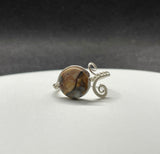 This unique ring showcases a stunning Venus Jasper gemstone, meticulously wrapped in high-quality Argentium silver wire for a sleek and contemporary design. The adjustable nature of the band allows it to fit comfortably for sizes 9 and up, making it perfect for a variety of hand sizes. Venus Jasper, known for its grounding properties and beautiful earthy tones, creates a striking contrast against the bright, tarnish-resistant Argentium silver.