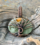 This Beautiful Blue Mountain Jasper Tree of Life Pendant is a captivating piece of jewelry featuring a striking Blue Mountain Jasper stone encased in intricate copper wirework. The pendant is designed with a Tree of Life motif, evoking imagery of a sun rising on a distant planet. This pendant combines natural beauty with symbolic craftsmanship, creating a unique and eye-catching accessory.