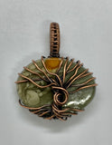 This Beautiful Blue Mountain Jasper Tree of Life Pendant is a captivating piece of jewelry featuring a striking Blue Mountain Jasper stone encased in intricate copper wirework. The pendant is designed with a Tree of Life motif, evoking imagery of a sun rising on a distant planet. This pendant combines natural beauty with symbolic craftsmanship, creating a unique and eye-catching accessory.