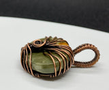 This Beautiful Blue Mountain Jasper Tree of Life Pendant is a captivating piece of jewelry featuring a striking Blue Mountain Jasper stone encased in intricate copper wirework. The pendant is designed with a Tree of Life motif, evoking imagery of a sun rising on a distant planet. This pendant combines natural beauty with symbolic craftsmanship, creating a unique and eye-catching accessory