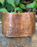 This striking wide copper cuff bracelet is hand-embossed with intricate patterns. The rich, warm tones of the copper are enhanced by the detailed embossing, creating a bold yet elegant statement piece.x